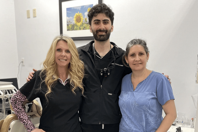 Three dental professionals smiling together in a treatment room in New Port Richey, FL.
